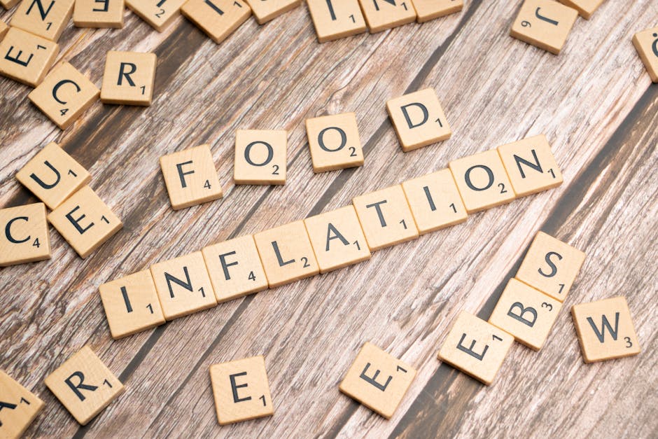 The image displays a series of light wooden Scrabble tiles arranged on a weathered wooden surface, spelling out the word 'INFLATION' in the center. Surrounding this main word are additional tiles with